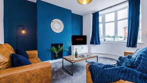 Una sala de estar con pared azul, chimenea, televisor y un ventanal con cortinas.