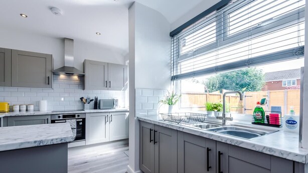 Una cocina moderna con armarios grises, encimera de mármol y ventana con persianas.