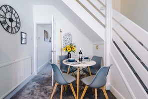 A dining area with a round table, four chairs, a vase with sunflowers, a bottle, and a clock on the wall. - Fresh House Amazing Location Great for Couples (Chester)