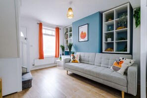 A living room with a sofa, a coffee table, a bookshelf, and a window with curtains. - Stylish Home Incredible Location Sleeps 5 (Chester)