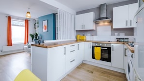 A modern kitchen with white cabinets, a wooden countertop, a built-in oven, and a yellow towel hanging on the oven handle. - Stylish Home Incredible Location Sleeps 5 (Chester)
