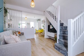 A modern living room with a sofa, a dining area with yellow chairs, a staircase, and a TV on a stand. - Stylish Home Incredible Location Sleeps 5 (Chester)