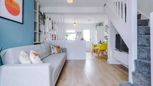 A modern living room with a sofa, a dining area with yellow chairs, and a staircase. - Stylish Home Incredible Location Sleeps 5 (Chester)