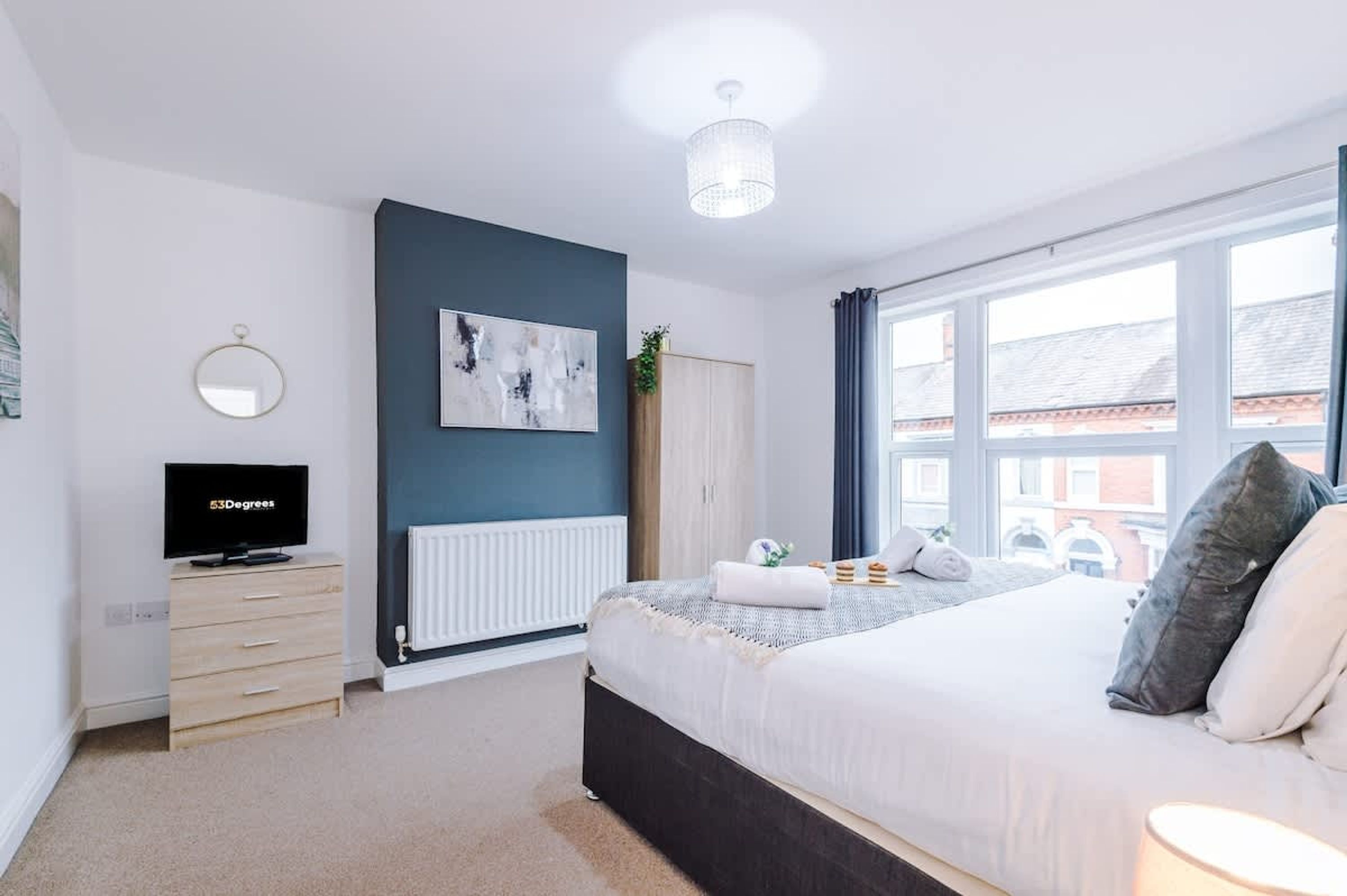 A modern bedroom with a bed, a TV, a radiator, and a window.