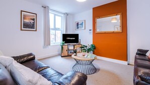 A living room with a sofa, a coffee table with drinks, a TV, and a window with curtains. - Modern Apartment Ideal for Business Sleeps 3 (Crewe)