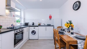 A compact kitchen with a dishwasher, oven, and washing machine. A dining table with chairs and a vase of sunflowers is set up. - Modern Apartment Ideal for Business Sleeps 3 (Crewe)
