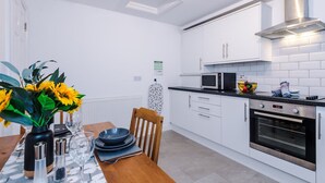 A modern kitchen with white cabinets, a microwave, an oven, and a dining table with a vase of sunflowers. - Modern Apartment Ideal for Business Sleeps 3 (Crewe)