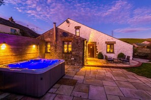 Une maison en pierre dotée d’un jacuzzi, d’un espace salon extérieur et d’une terrasse bien éclairée.