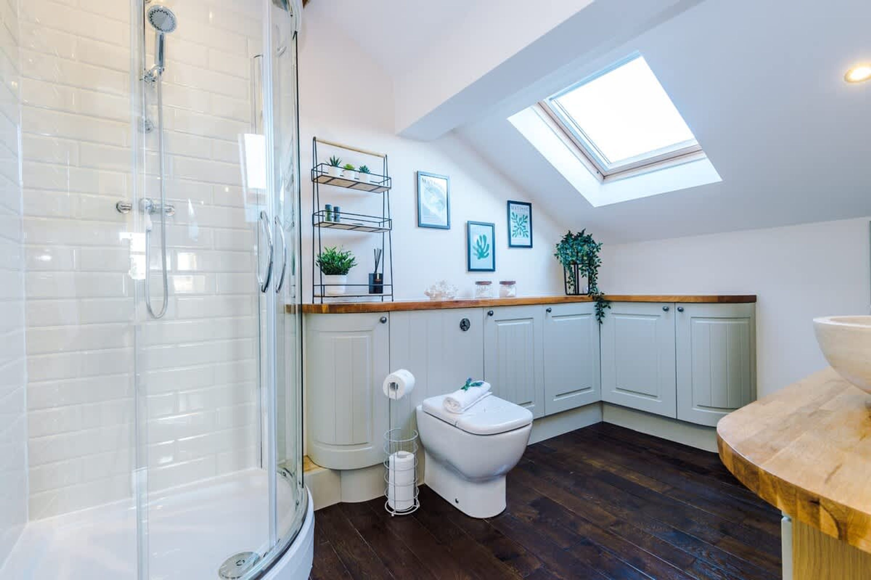 A modern bathroom with a glass shower enclosure, a toilet, a sink, and a skylight.
