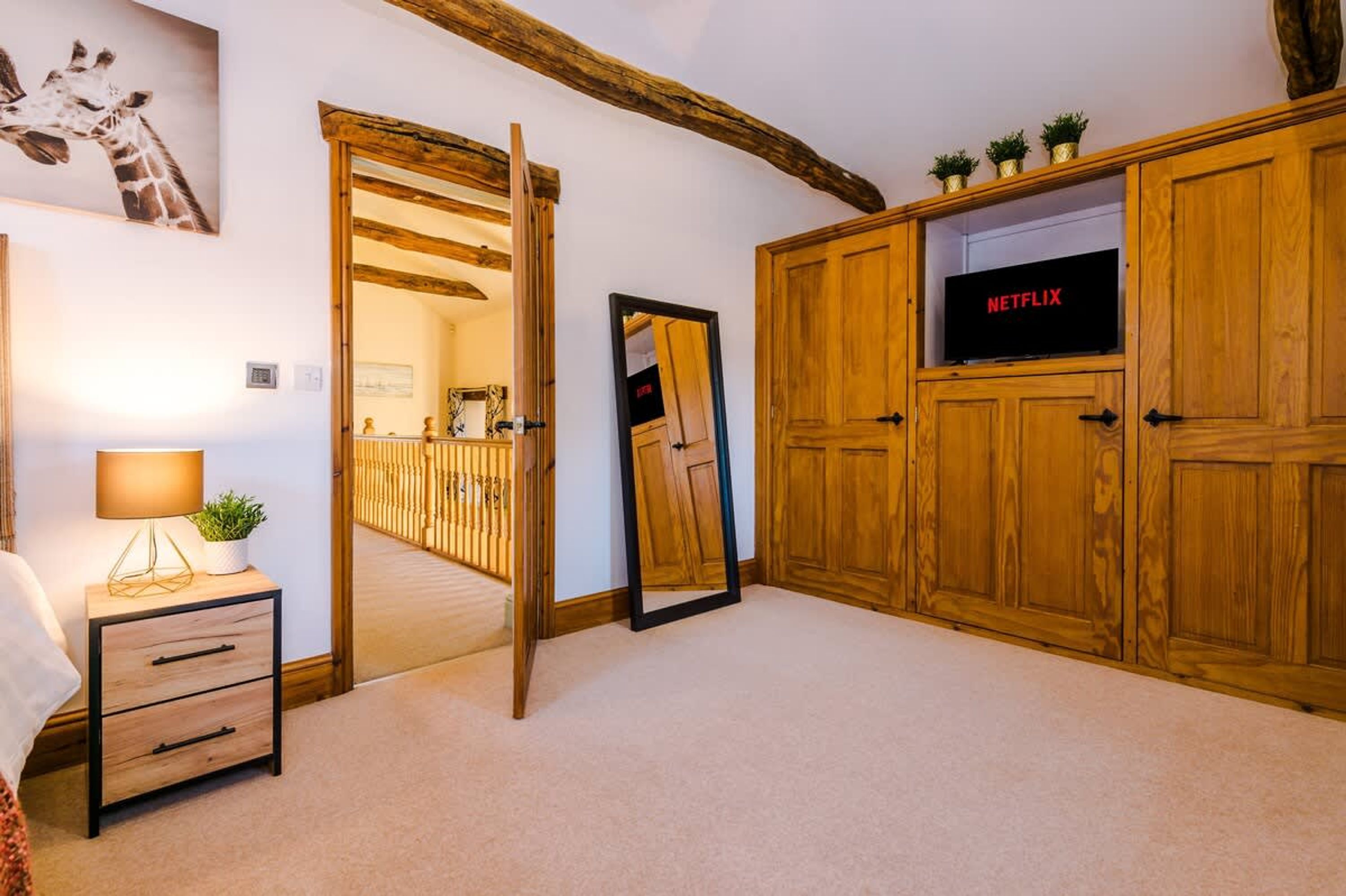 Une chambre avec une armoire en bois, une table de chevet avec une lampe, un miroir et un téléviseur affichant le logo « NETFLIX ».