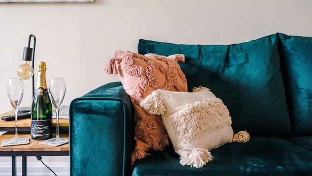 Ein türkisfarbenes Sofa mit zwei Zierkissen, einer Champagnerflasche und zwei Gläsern auf einem Holztisch.