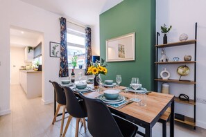 A dining area with a wooden table set for four, black chairs, a vase with sunflowers, and a green accent wall. - Stunning 3-bed House Amazing Location Sleeps 5 (Nantwich)