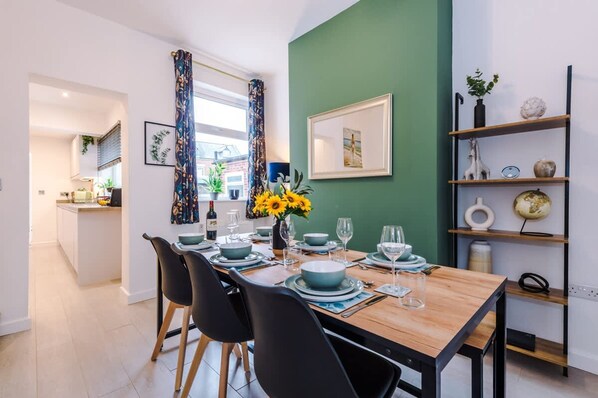 A dining area with a wooden table set for four, black chairs, a vase with sunflowers, and a green accent wall.