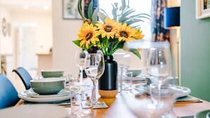 A dining table set with plates, bowls, and wine glasses, with a vase of sunflowers in the center. - Stunning 3-bed House Amazing Location Sleeps 5 (Nantwich)