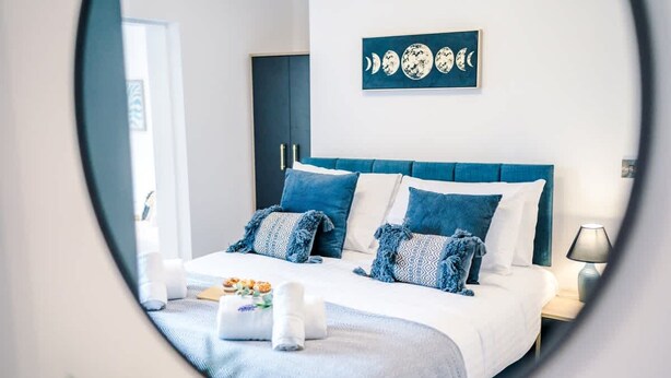 A neatly made bed with blue and white bedding, a wall-mounted artwork of moon phases, and a bedside lamp. - Stunning 3-bed House Amazing Location Sleeps 5 (Nantwich)