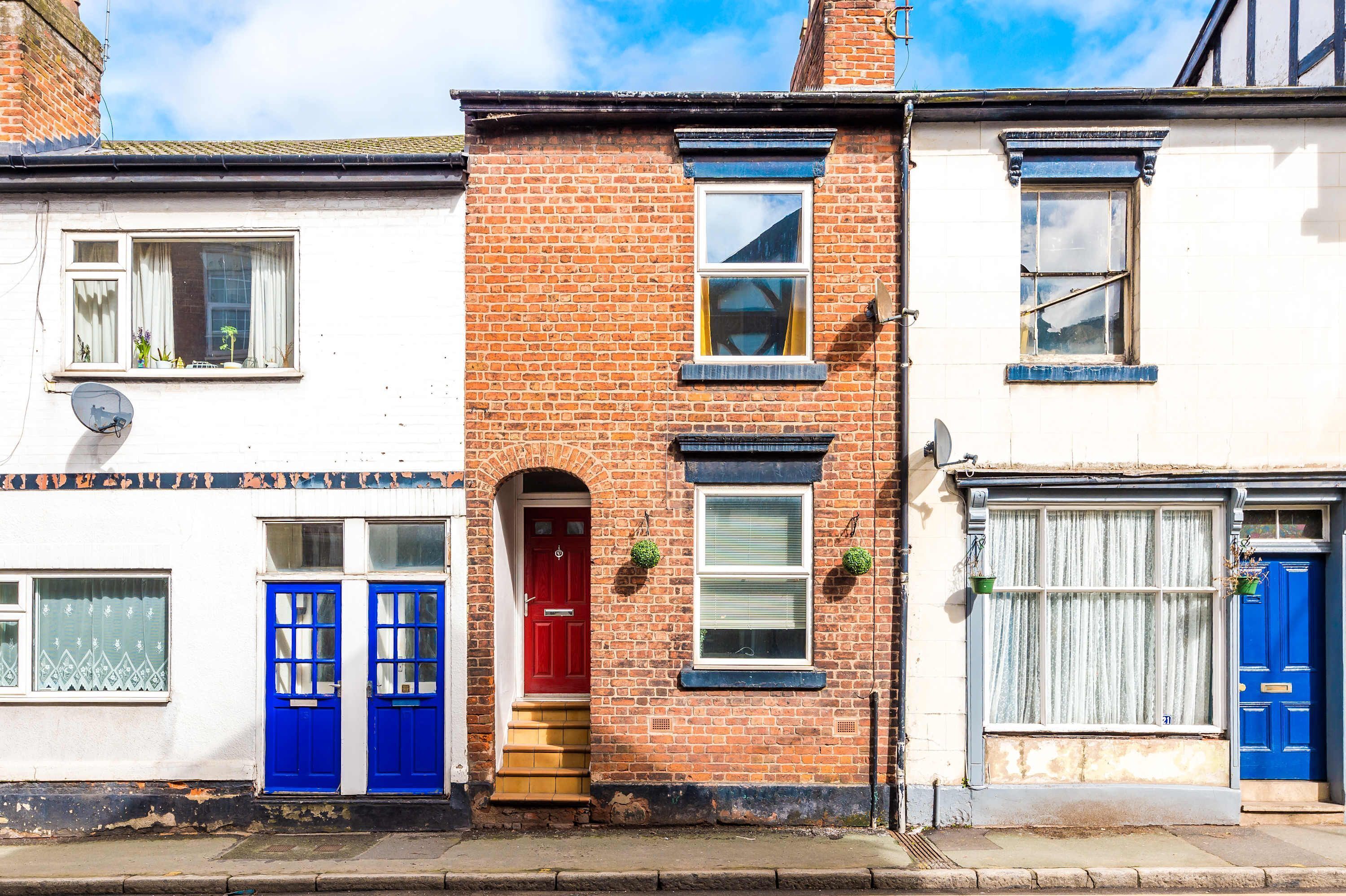 A row of terraced houses with distinct red brick facades, white walls, and blue doors.