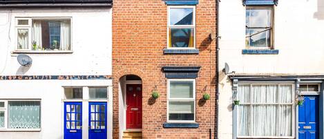 A row of terraced houses with distinct red brick facades, white walls, and blue doors.