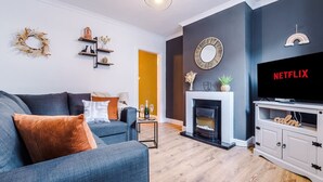 Una sala de estar con chimenea, televisor y estantería.