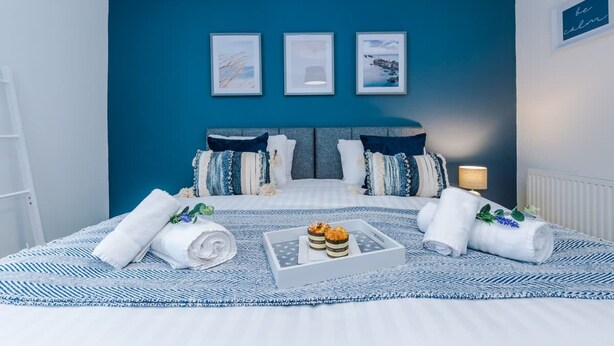 Un dormitorio con cama, almohadas, una bandeja con toallas y un objeto pequeño, y cuadros en la pared.