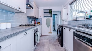 Una cocina moderna con armarios blancos, estufa integrada, lavavajillas y ventana con persianas.