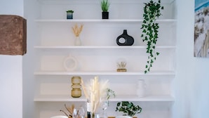A white shelf with various decorative items, a dining table with plates and glasses, and a painting on the wall. - Lovely House Great Location Perfect for Couples (Chester)