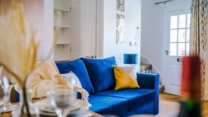 A living room with a blue sofa, a white door, and a window with curtains. - Lovely House Great Location Perfect for Couples (Chester)