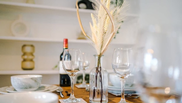 A dining table set with clear glassware, a vase with dried flowers, and a bottle of wine. - Lovely House Great Location Perfect for Couples (Chester)