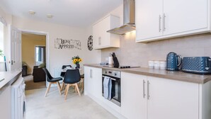 Uma cozinha moderna com armários brancos, forno embutido, cafeteira e um espaço de jantar com mesa e cadeiras.