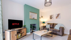 Uma sala de estar com televisão, sofá, mesa de centro e lareira.