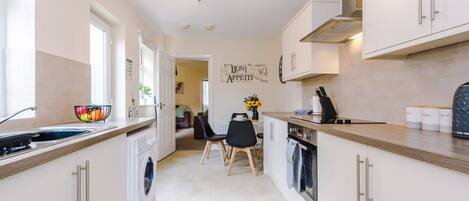 A modern kitchen with a washing machine, a dining area with chairs, and a wall with a decorative sign.