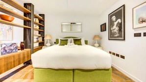 A modern hotel room with a large bed, a wooden bookshelf, a mirror, and artwork on the walls. - Pristine Studio Incredible Location Long Stays (London)