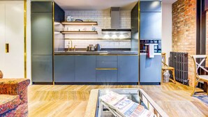 A modern kitchen with a central island, built-in appliances, and a brick accent wall. - Pristine Studio Incredible Location Long Stays (London)