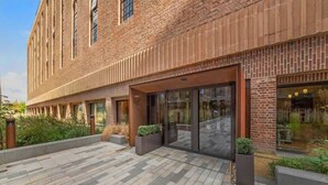 A modern building with a brick facade, large glass windows, and a paved outdoor area with planters. - Pristine Studio Incredible Location Long Stays (London)