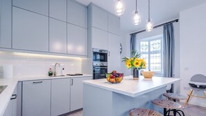 A modern kitchen with grey cabinets, a central island with stools, an oven, and a window with curtains. - New Stylish City-centre Flat w Parking Sleeps 4 (Birmingham)