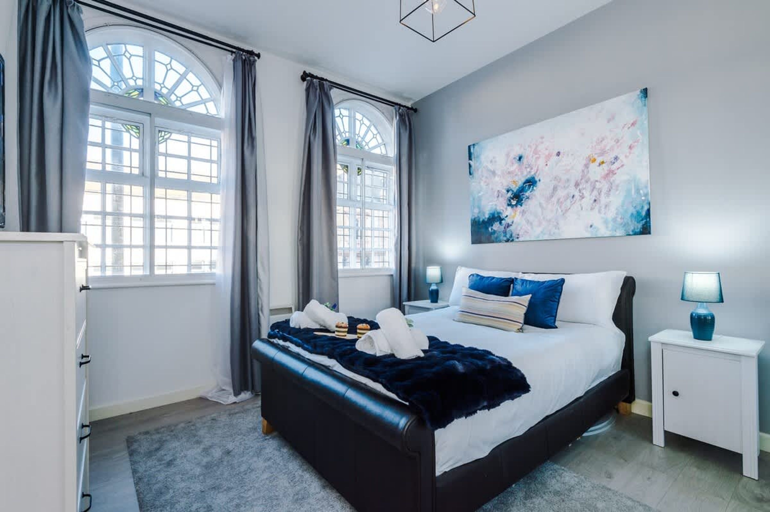 A modern bedroom with a large bed, two bedside tables, a nightstand, and a window with curtains.