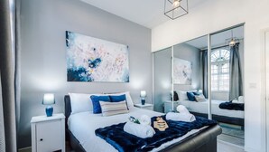 A modern bedroom with a large bed, bedside tables, a mirror, and abstract art on the wall. - New Stylish City-centre Flat w Parking Sleeps 4 (Birmingham)
