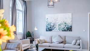 A modern living room with a sofa, a coffee table, and a large abstract painting on the wall. - New Stylish City-centre Flat w Parking Sleeps 4 (Birmingham)