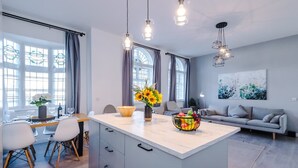 A modern kitchen with a central island, dining area, and a living space with a sofa and artwork. - New Stylish City-centre Flat w Parking Sleeps 4 (Birmingham)