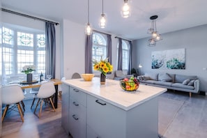 A modern kitchen with a central island, dining area, and a living space with a sofa and artwork. - New Stylish City-centre Flat w Parking Sleeps 4 (Birmingham)
