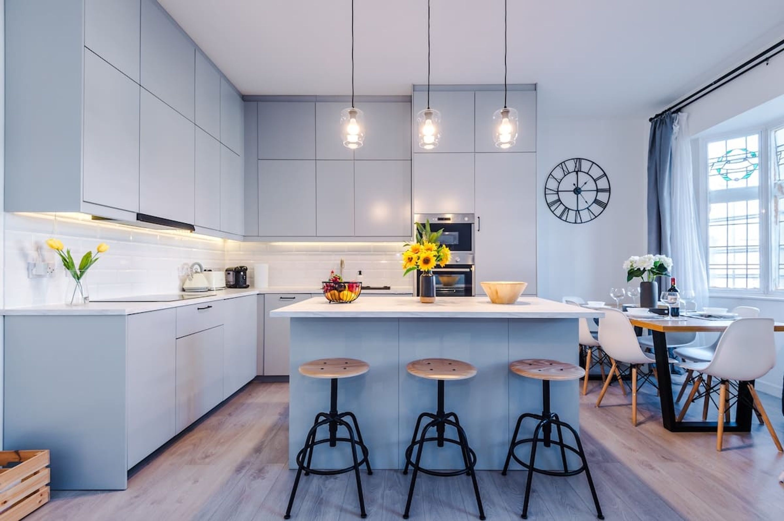 Een moderne keuken met een centraal eiland, barkrukken en een eethoek met stoelen en een tafel.
