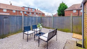 Eine Terrasse mit Gartenmöbeln, ein Holzzaun und ein Backsteingebäude im Hintergrund.