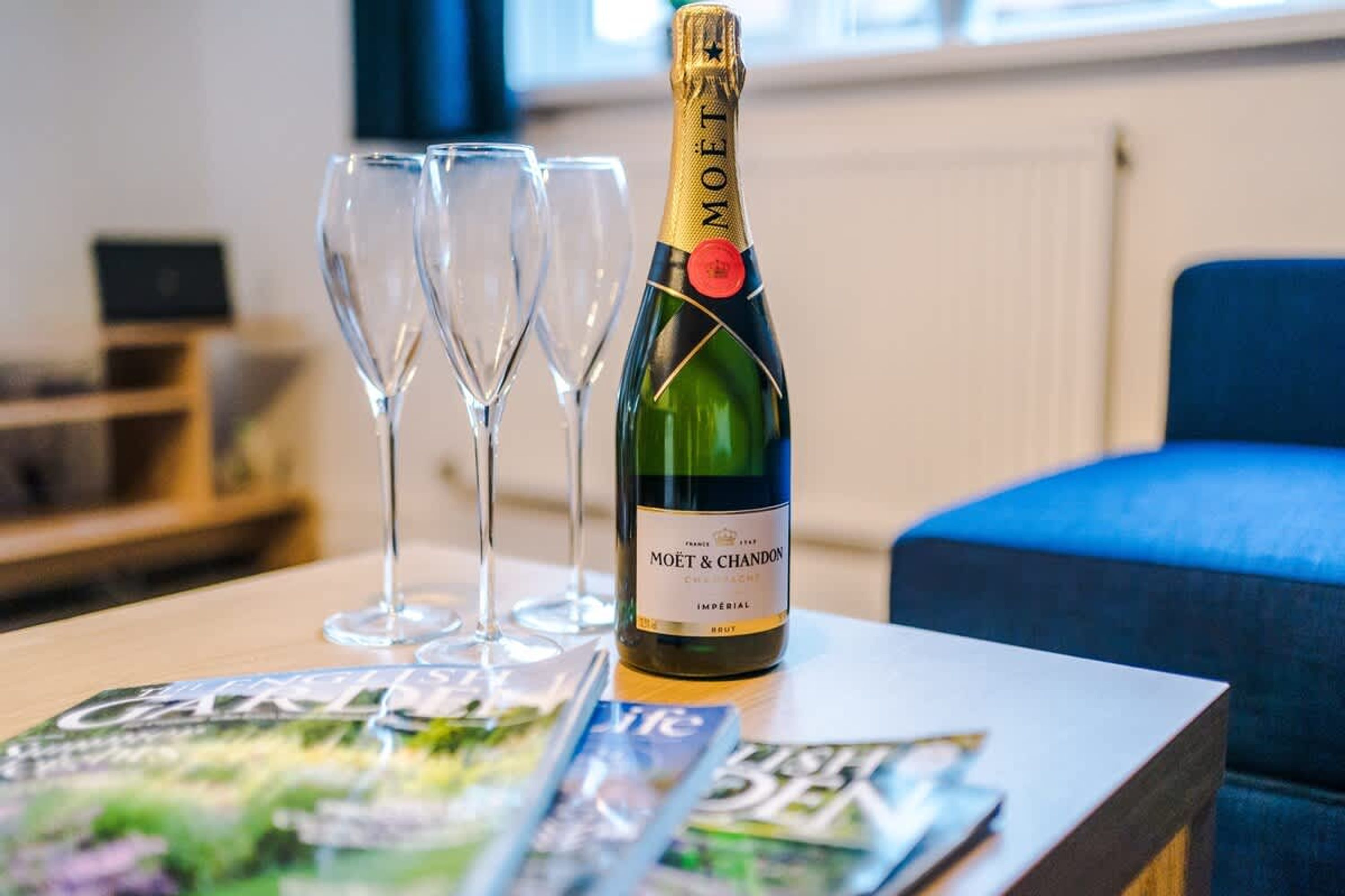 Una botella de champán Moët & Chandon sobre una mesa con tres copas vacías y revistas.