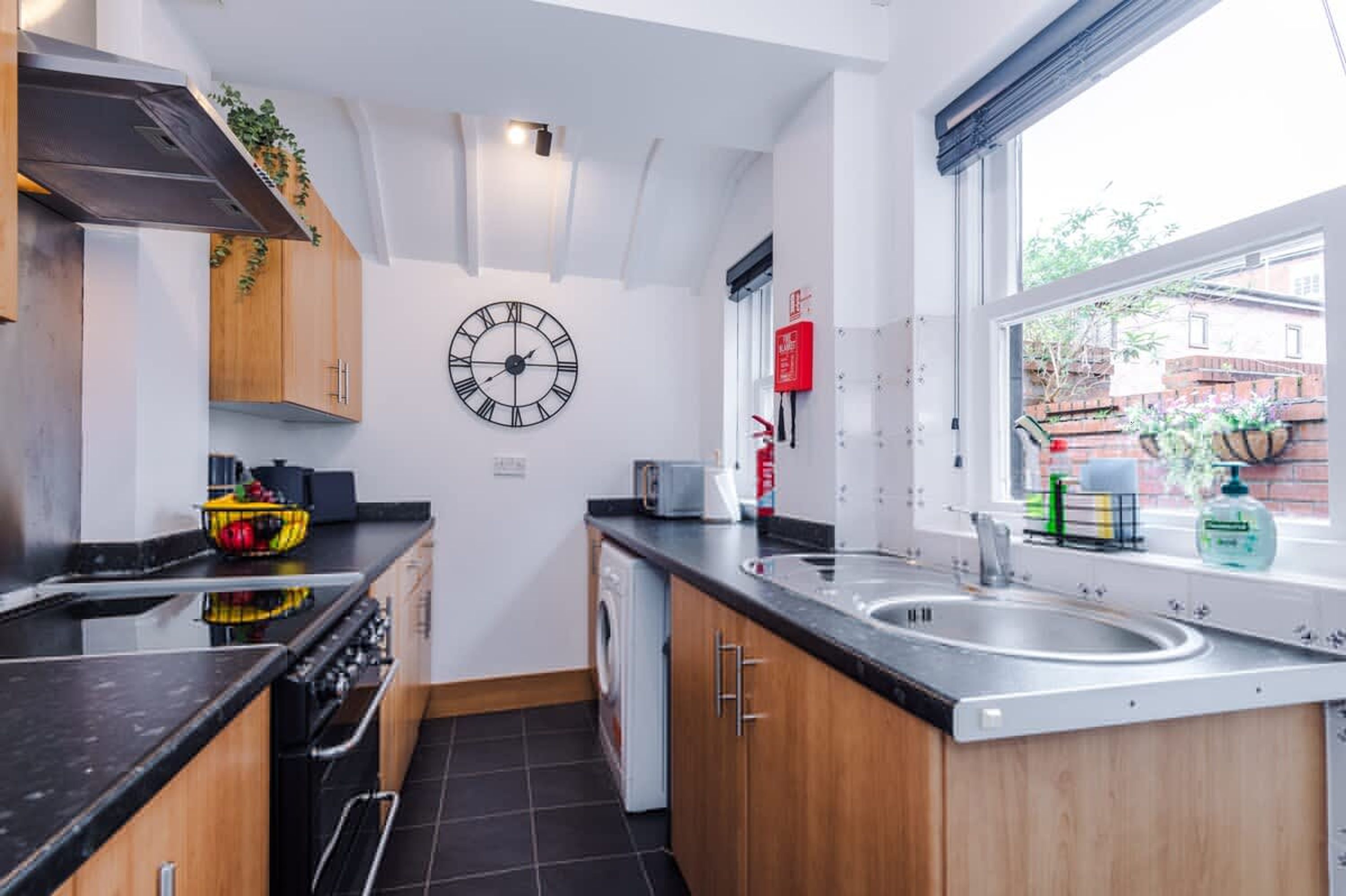A modern kitchen with a black countertop, wooden cabinets, a stainless steel sink, and a clock on the wall.