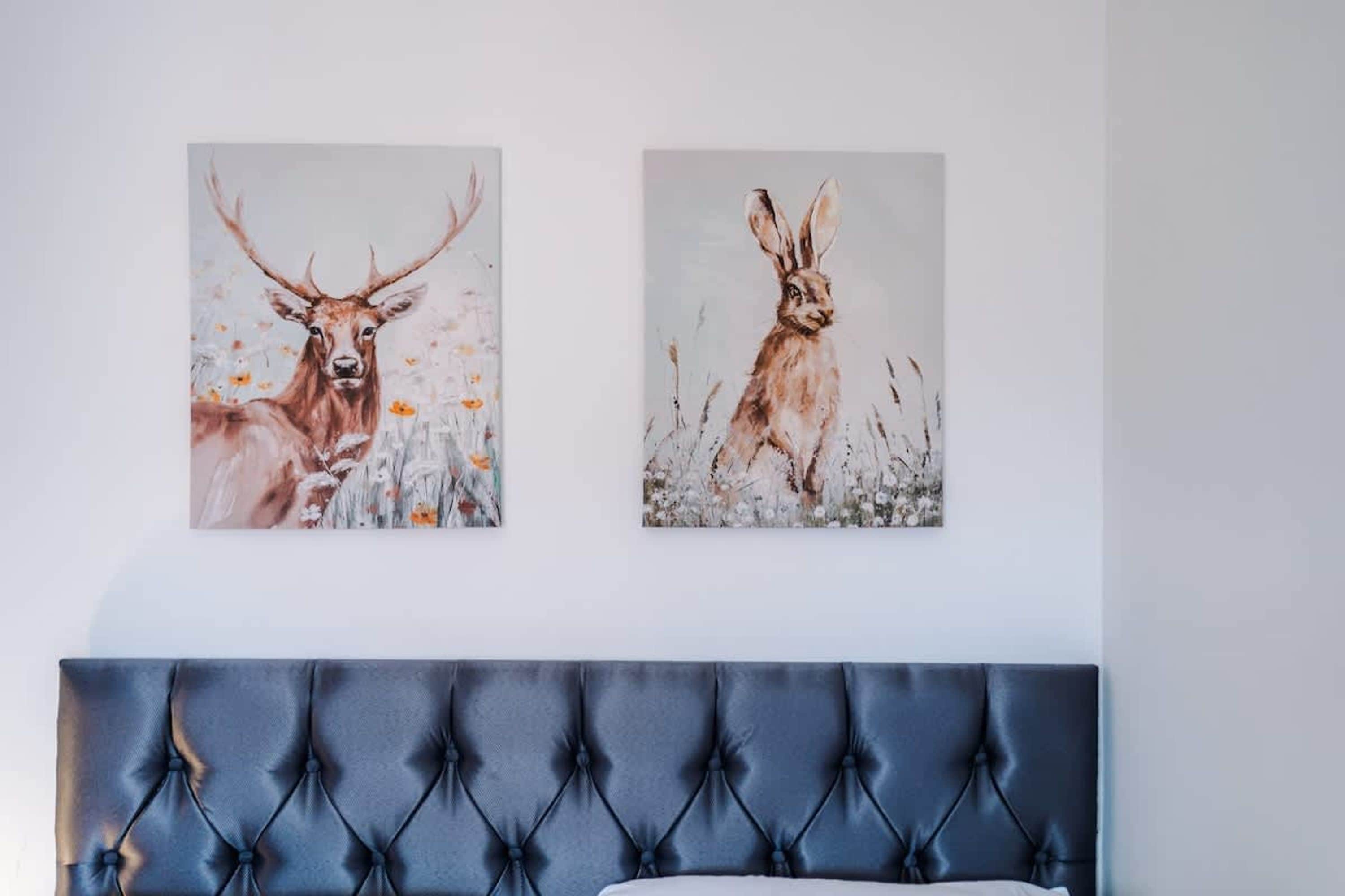 Une chambre à coucher avec une tête de lit capitonnée, deux tableaux encadrés représentant des animaux sauvages et un couvre-lit blanc.