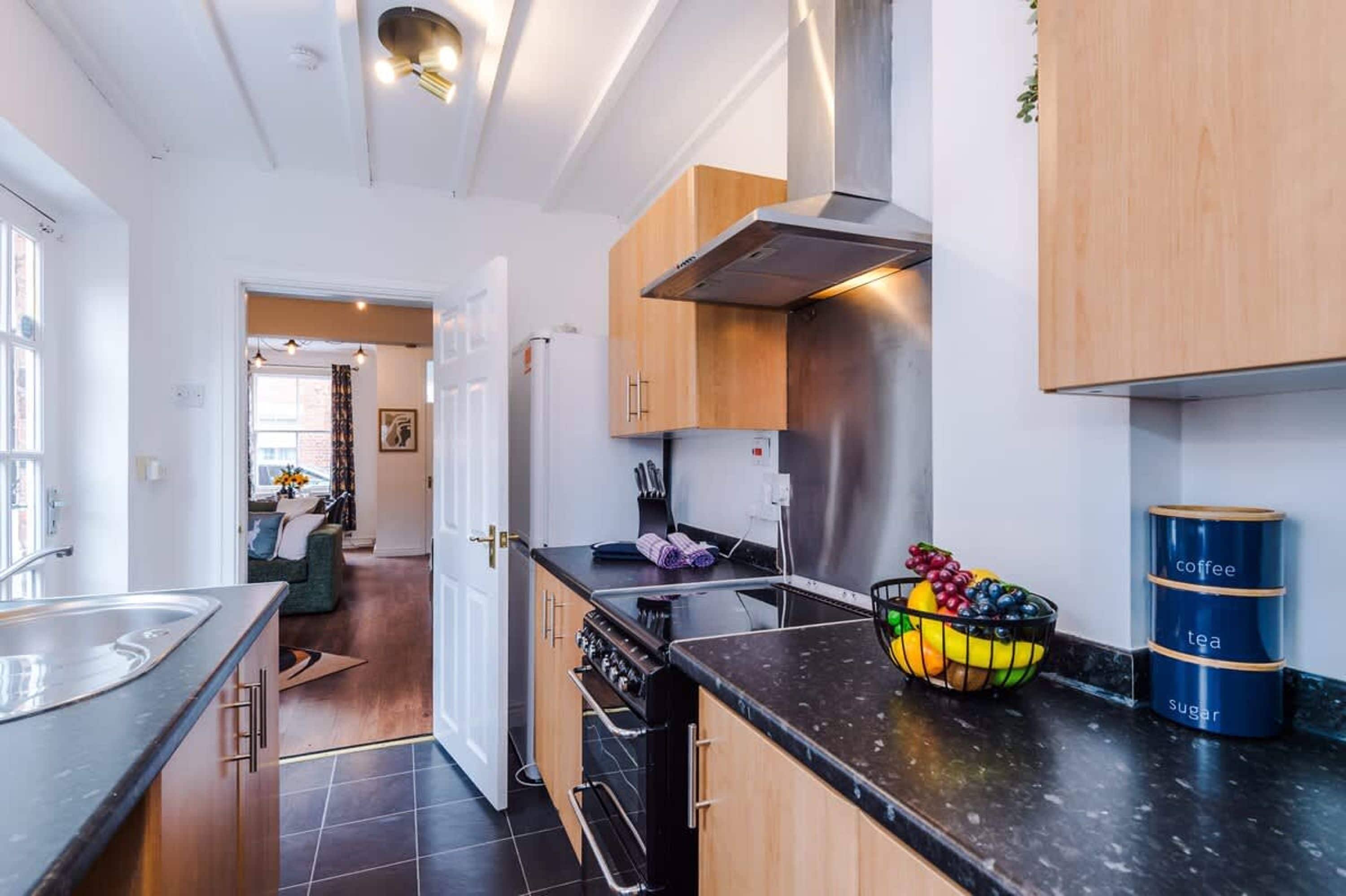 Une cuisine moderne équipée d’une cuisinière, d’un four et d’un panier de fruits posé sur le plan de travail.