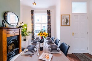 A dining room with a wooden table set for six, a fireplace, a large mirror, and a window with curtains. - NEW Stylish City Centre Home Great Location (Chester)