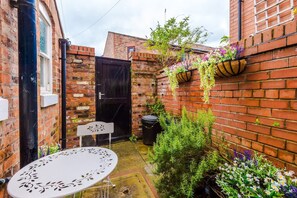 A brick building with a black door, a white table, and hanging flower baskets.