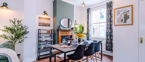A dining area with a wooden table, black chairs, a vase with sunflowers, a mirror, and a bookshelf.