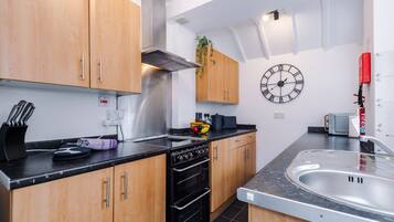 Une cuisine moderne avec des meubles en bois, une hotte en acier inoxydable, un four noir, un évier et une horloge murale.