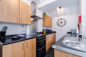 A modern kitchen with wooden cabinets, a stainless steel range hood, a black oven, a sink, and a wall clock.